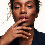 Held Ring – worn with a fingertip resting on the lips, gold, dark blazer, ivory studio background