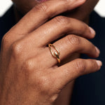 Held Ring – worn with the fingers resting at the chin, close-up, gold, dark blazer, ivory studio background