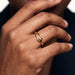 Held Ring – worn with the fingers resting at the chin, close-up, gold, dark blazer, ivory studio background