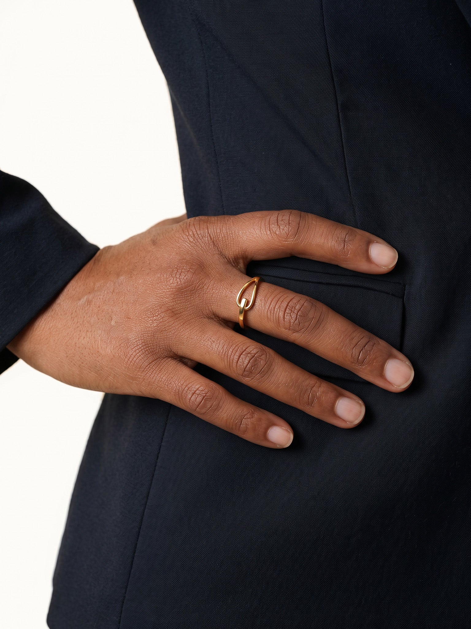 Held Ring – worn with the hand resting on the hip, gold, dark blazer, ivory studio background