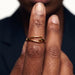 Held Ring – worn on fingers raised in front of the lips, close-up, gold, dark blazer, ivory studio background