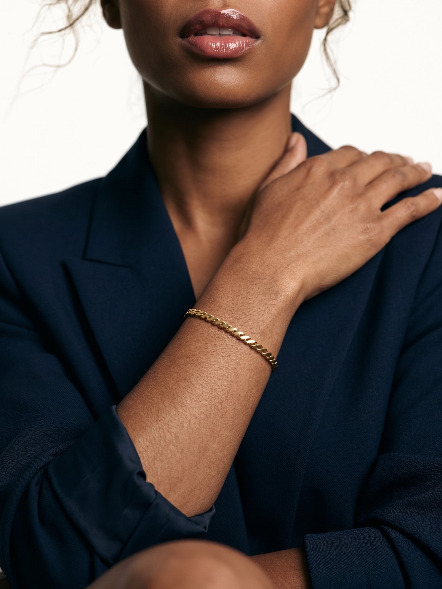 Kept Season Bangle – worn on the wrist, hand resting on the shoulder, gold, dark blazer, ivory studio background