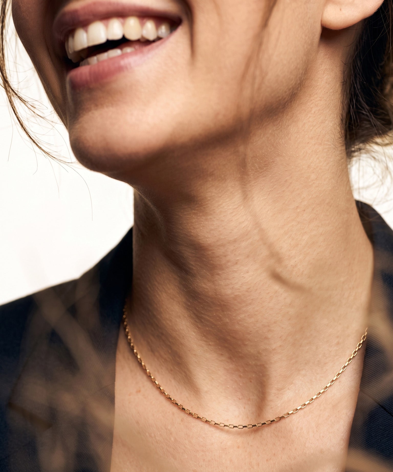 Kindred Link Necklace – worn at the collarbone, laughing, gold, navy blazer, ivory studio background