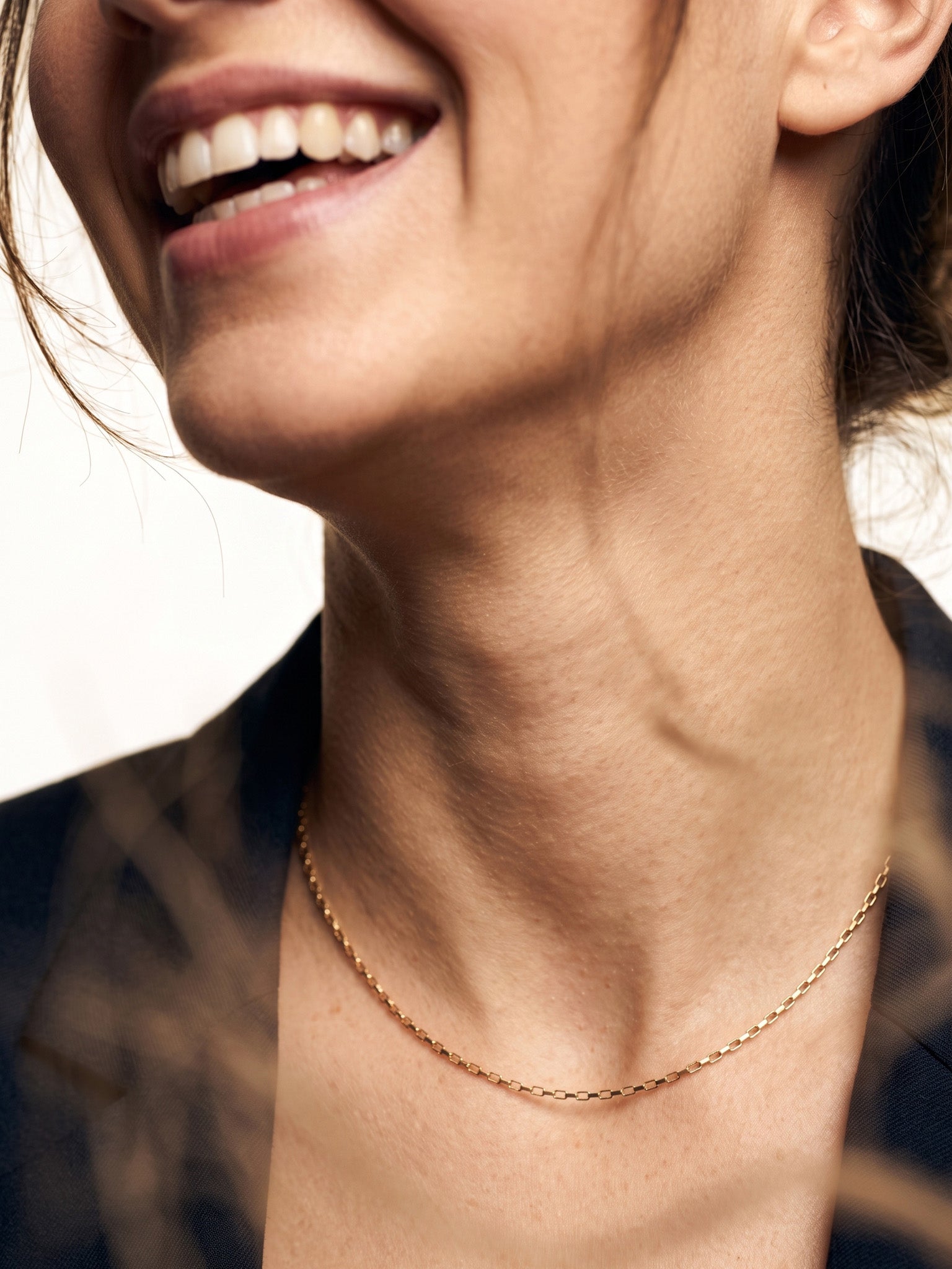 Kindred Link Necklace – worn at the collarbone, laughing, gold, navy blazer, ivory studio background