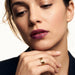 Mercies Ring – worn on a hand resting beneath the chin, gold, dark blazer, ivory studio background