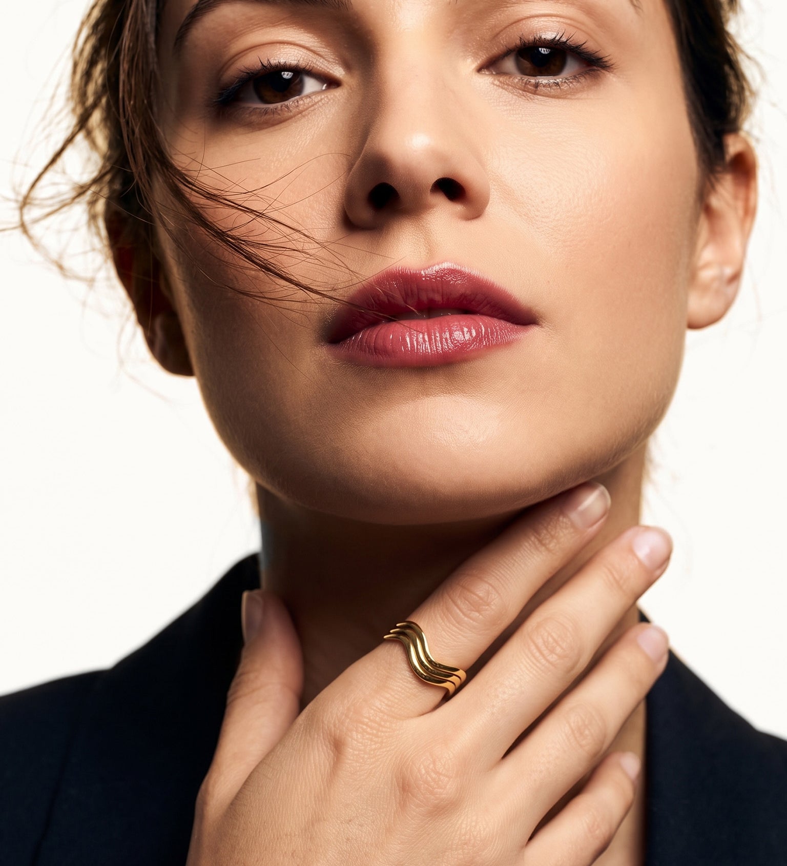 Mercies Ring – worn with the hand resting at the neck, gold, dark blazer, ivory studio background