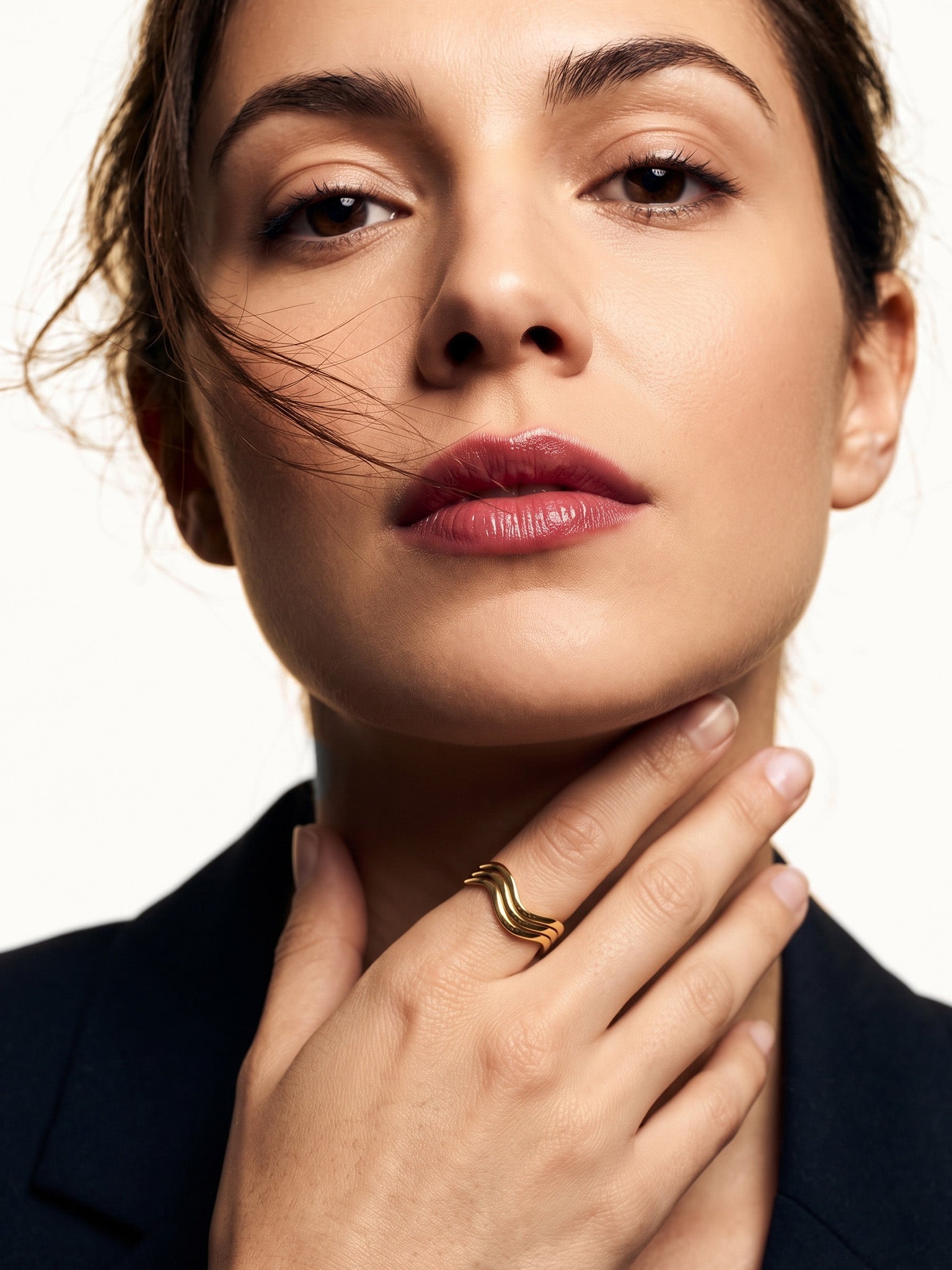 Mercies Ring – worn with the hand resting at the neck, gold, dark blazer, ivory studio background