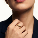 Mercies Ring – worn on a closed hand at the collarbone, gold, dark blazer, ivory studio background