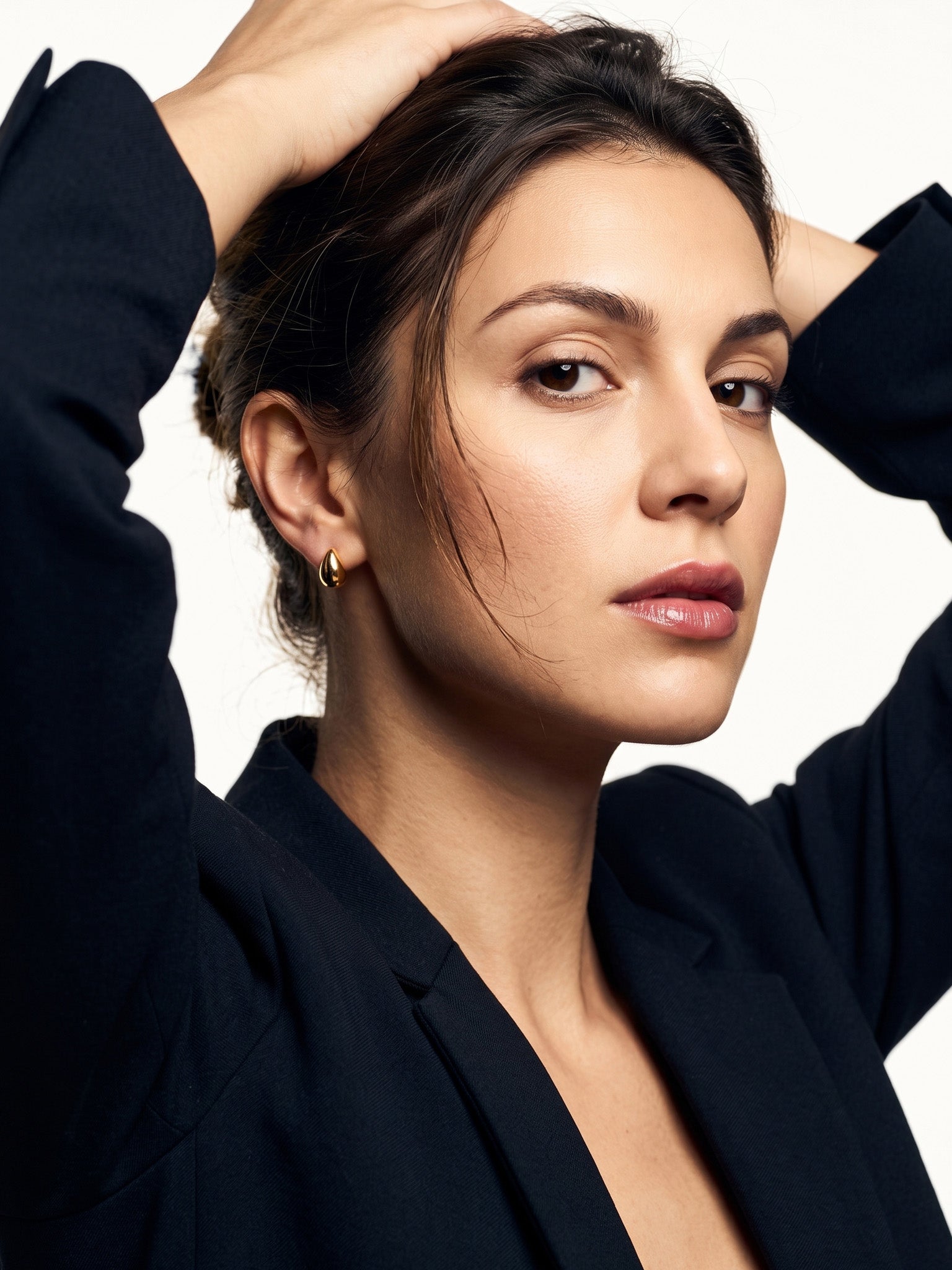 Morning Joy Studs – worn in the ear, both hands in the hair, looking at the camera, gold teardrop stud, dark hair up