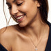 Radiant Cross Necklace – worn on the neck, looking down with a smile, gold cross with clear stones on a fine chain, bare shoulders