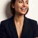 Radiant Cross Necklace – worn on the neck, smiling and looking aside with arms crossed, gold cross with clear stones on a fine chain