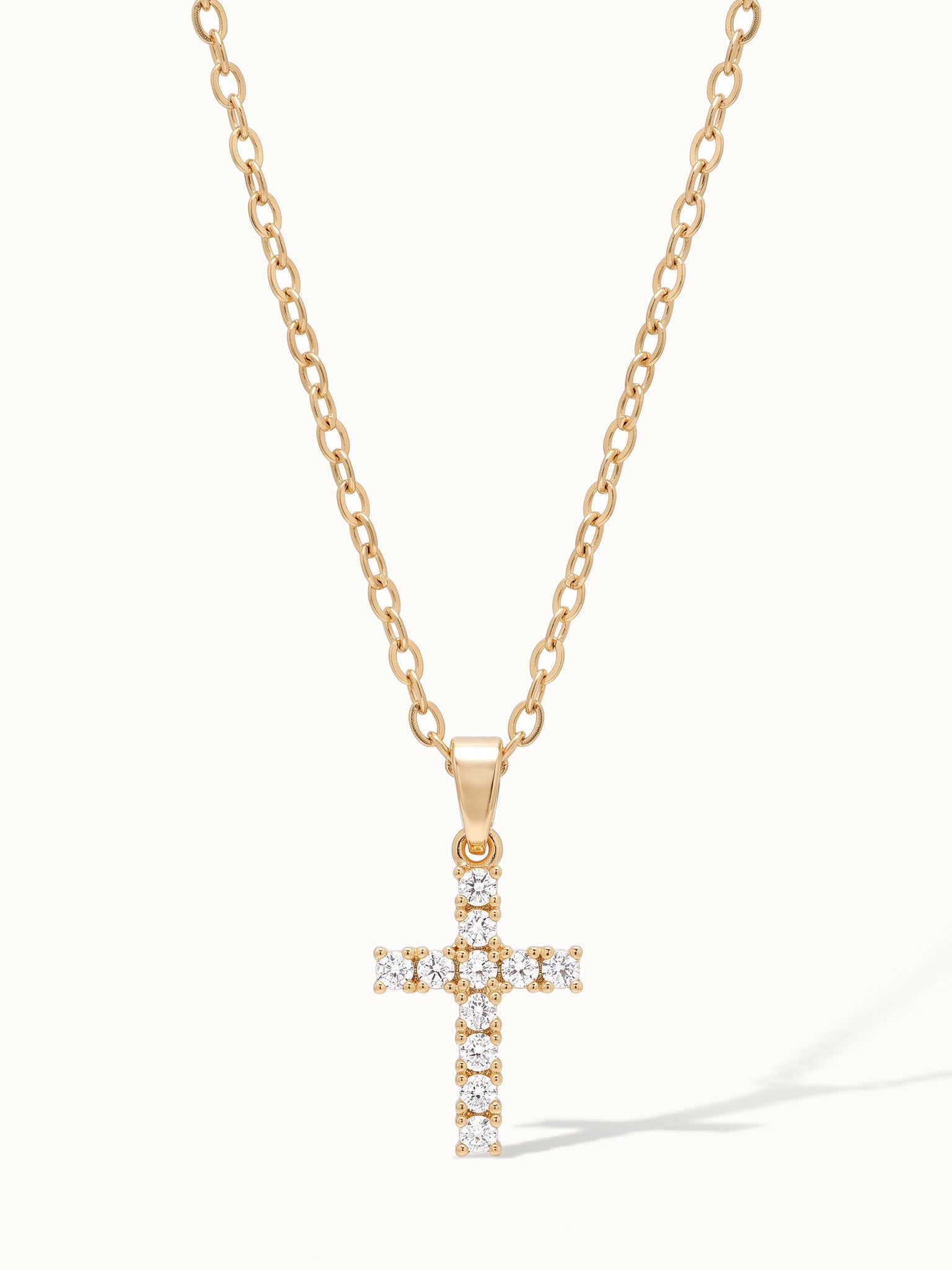 Radiant Cross Necklace in gold, hanging on a fine chain, with a long shadow
