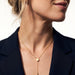 Rising Lariat Necklace – gold lariat with disc slider and bar drop worn on a model with her hair up, face turned, navy blazer