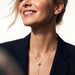 Rising Lariat Necklace – gold lariat with disc slider and bar drop worn by a smiling model with eyes closed, navy blazer