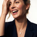 Rising Lariat Necklace – gold lariat with disc slider and bar drop worn by a laughing model with one hand in her hair, navy blazer