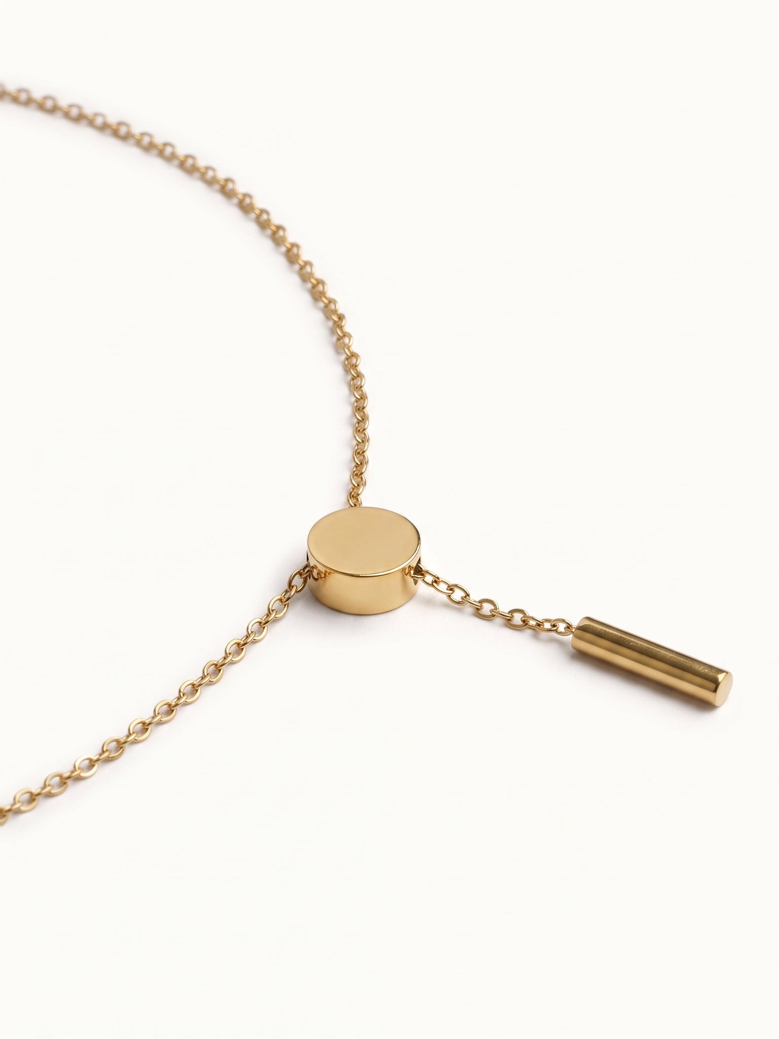 Rising Lariat Necklace – lariat laid in a curve with disc slider and bar drop, gold, on ivory background