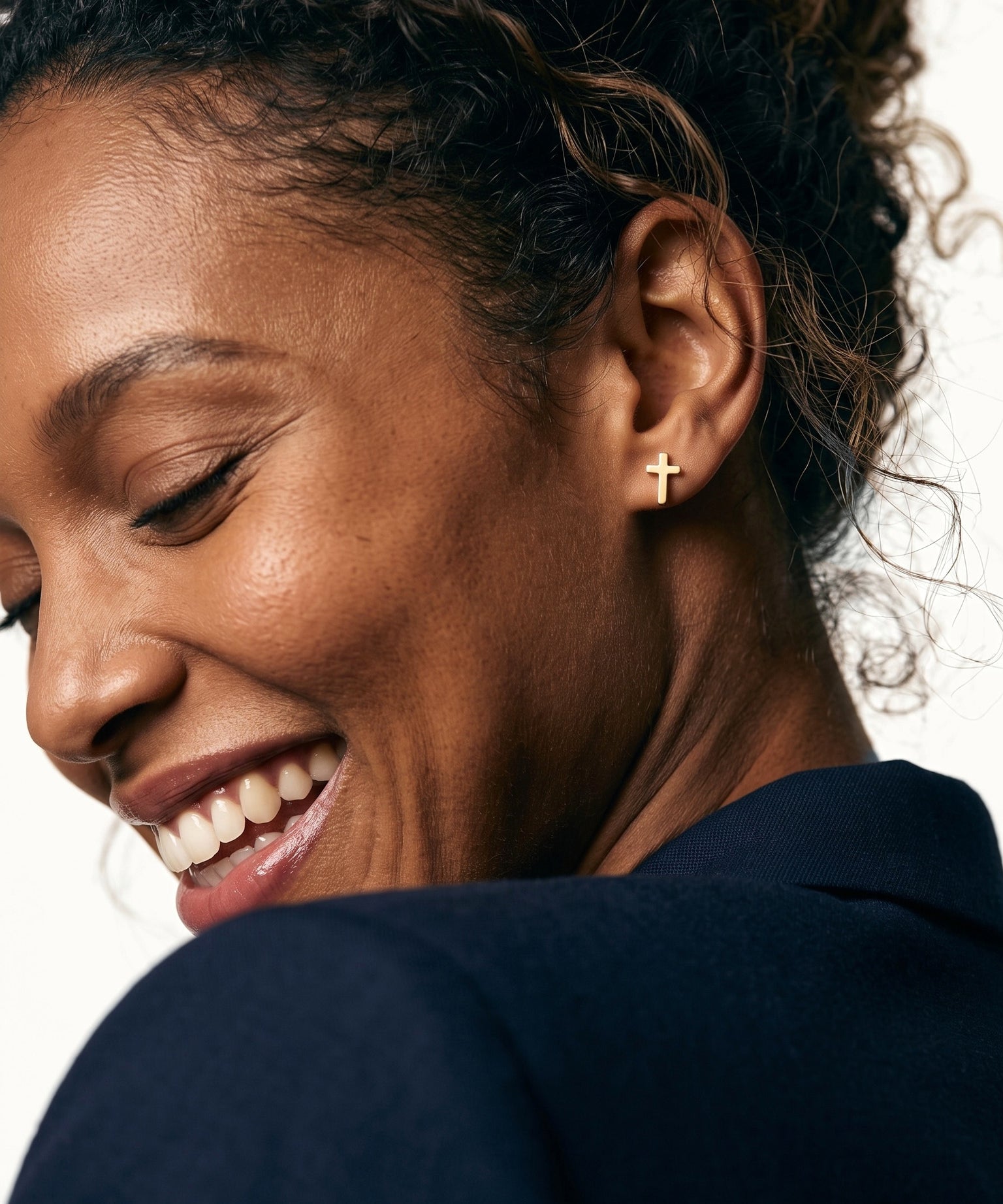 Rooted Cross Studs – worn in the ear, laughing with eyes closed and head tilted down, gold cross stud, curly hair up