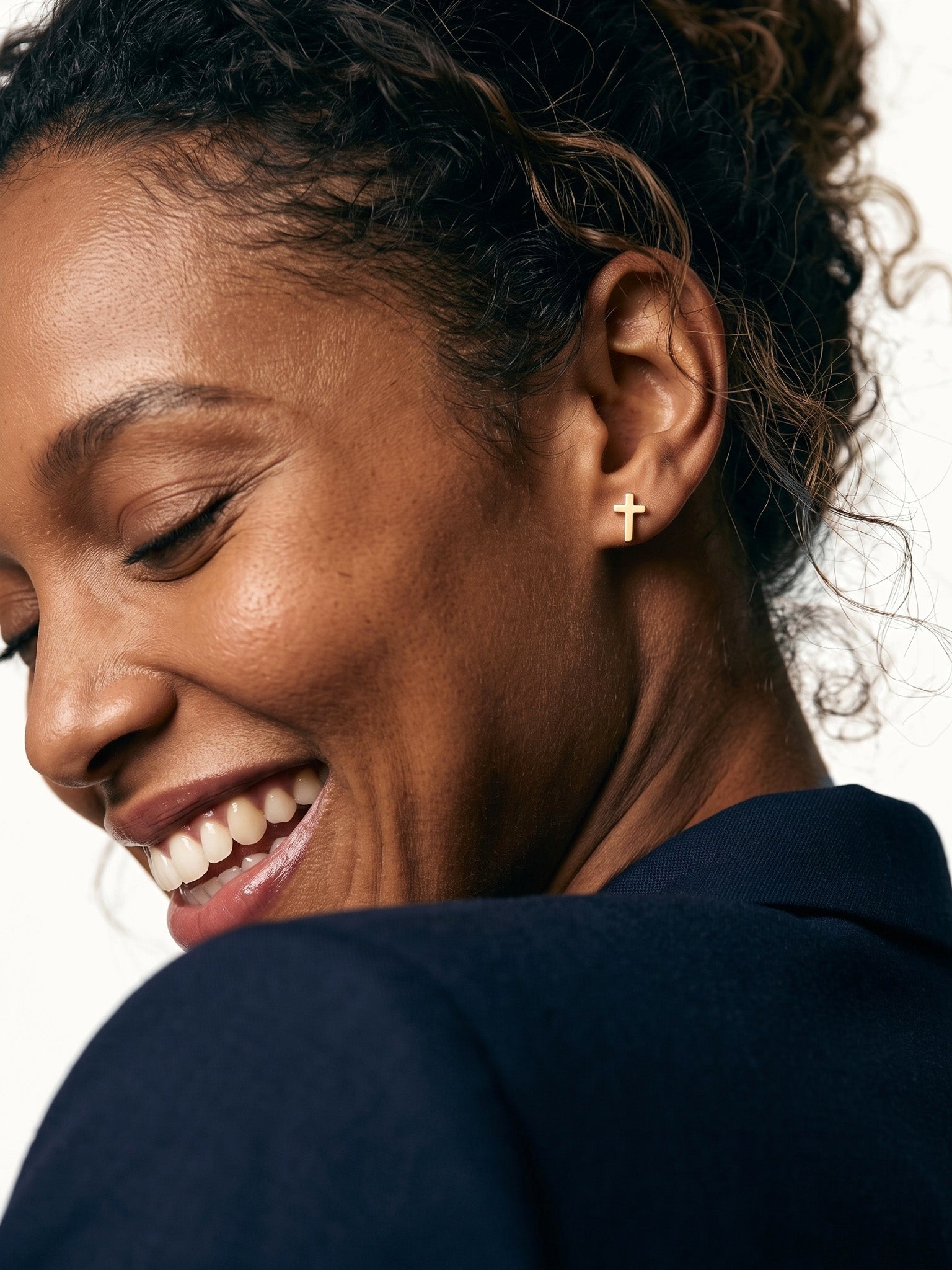 Rooted Cross Studs – worn in the ear, laughing with eyes closed and head tilted down, gold cross stud, curly hair up