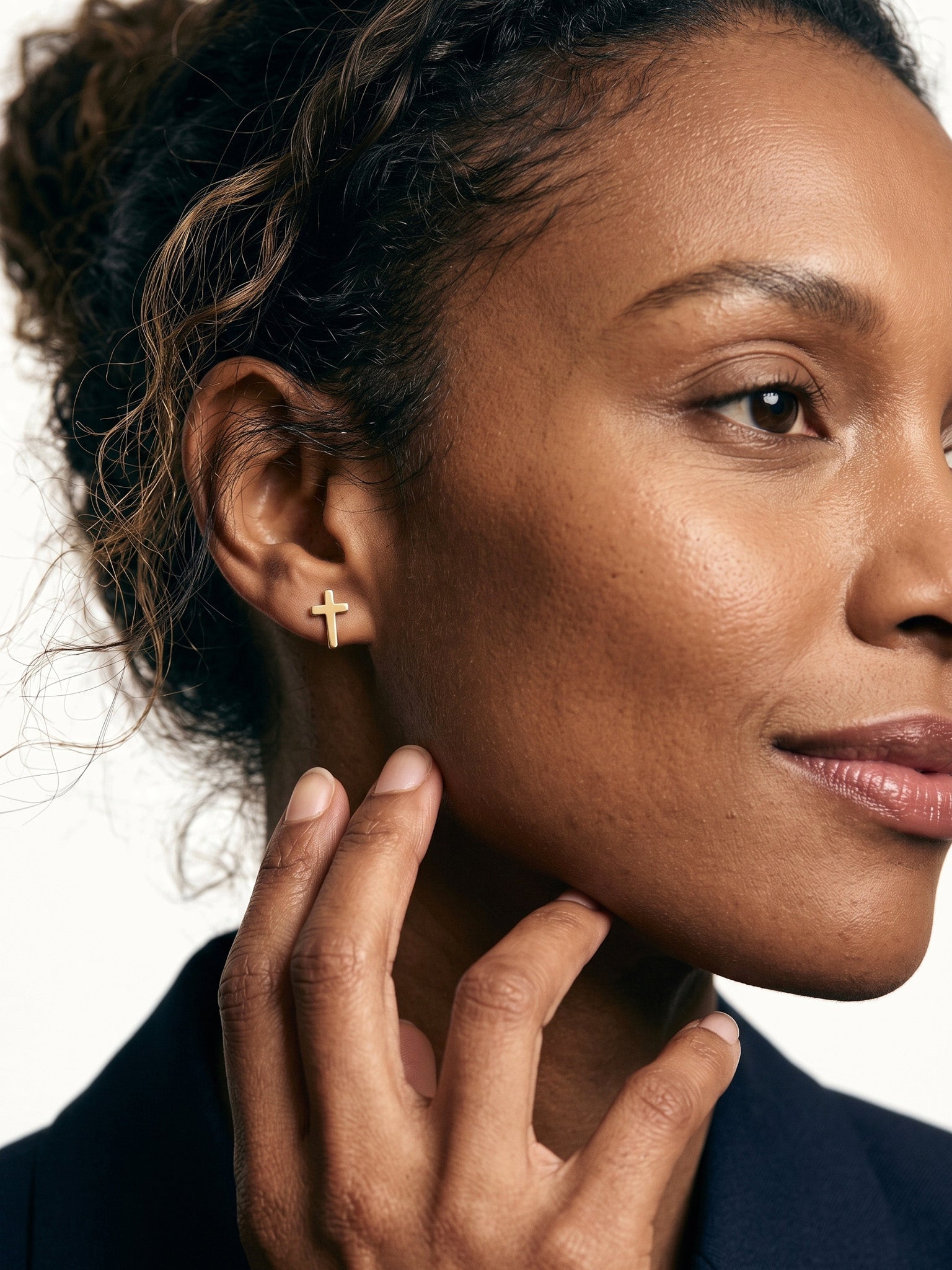 Rooted Cross Studs – worn in the ear, side profile with a hand at the jaw, gold cross stud, curly hair up