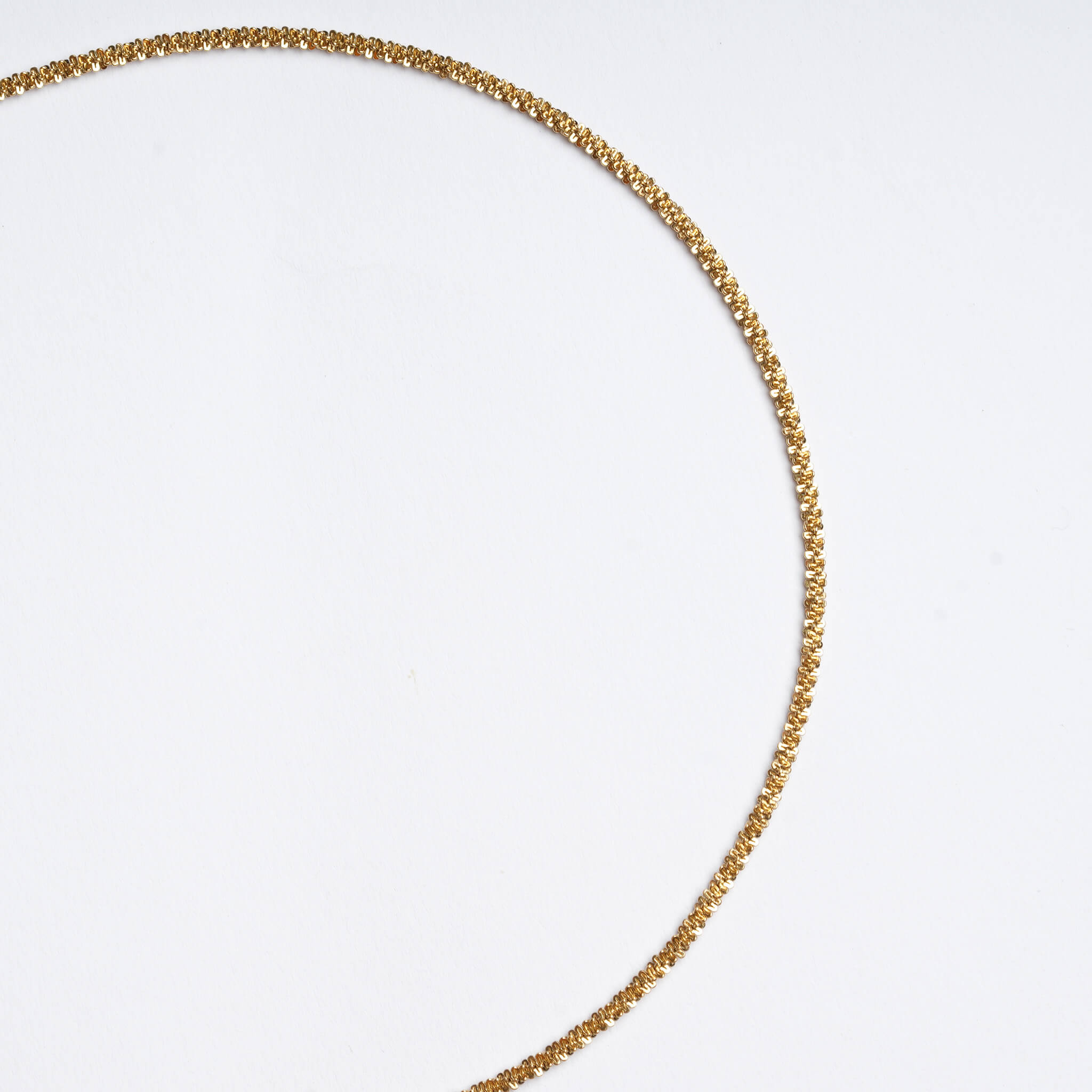 Rooted Rope Chain Necklace – braided rope chain curving across the frame, gold, on a pale grey background