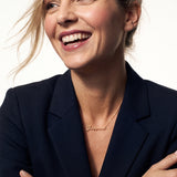 Signature Name Necklace – name "Jessica" in script at the collarbone, woman laughing and looking to one side, arms folded, gold, dark blazer, ivory studio background