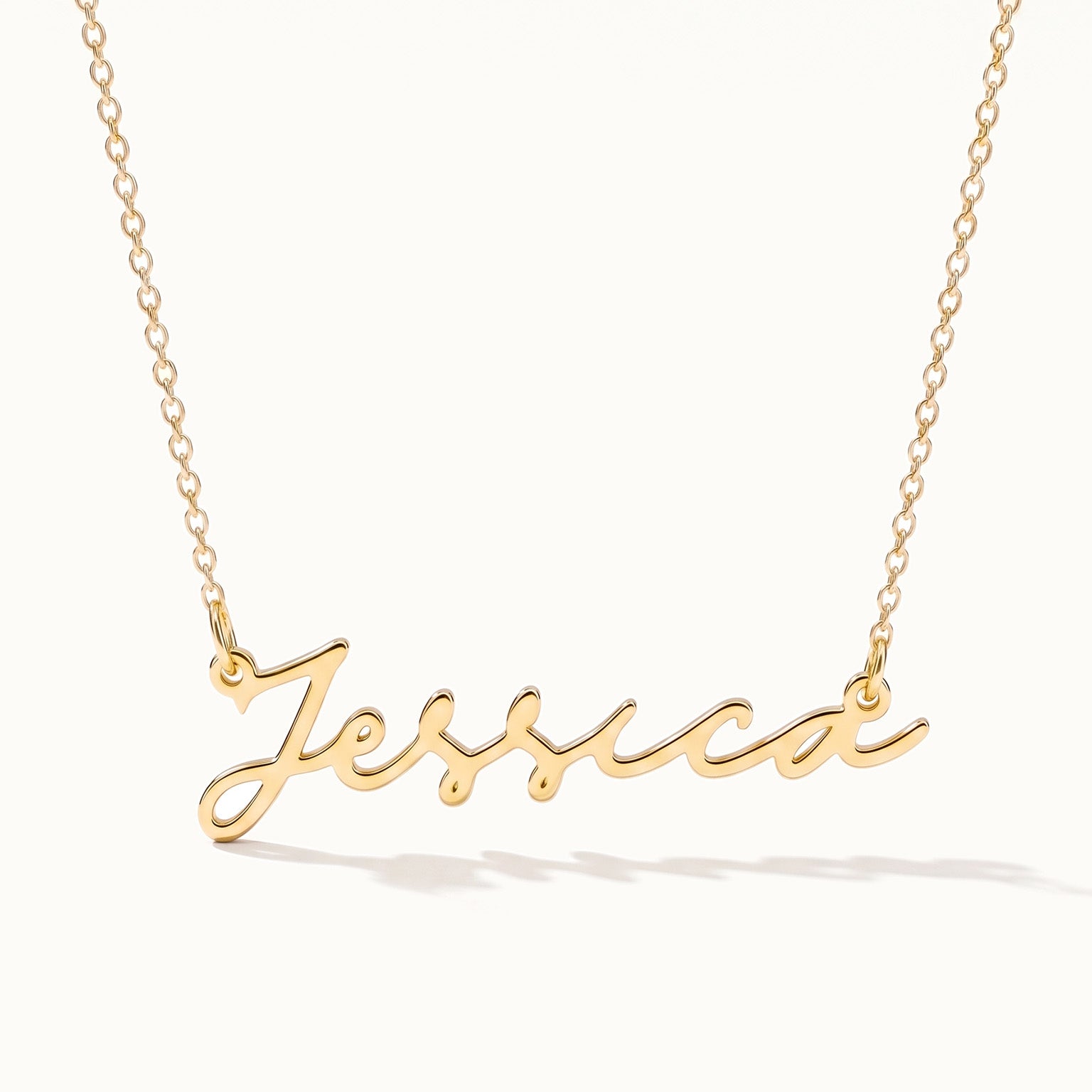 Signature Name Necklace – name "Jessica" in script hanging on a fine chain, closer view, gold, on ivory background
