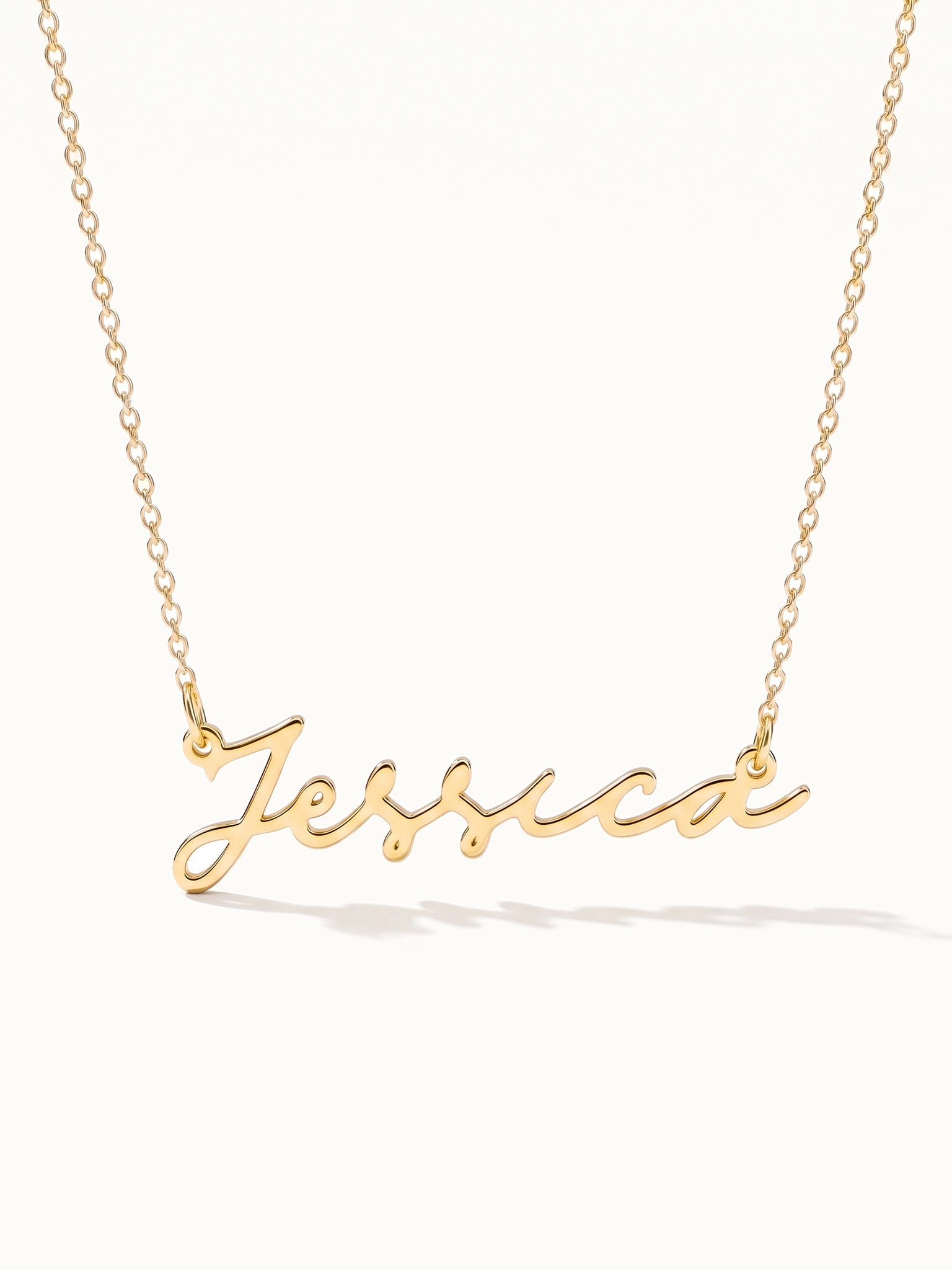 Signature Name Necklace – name "Jessica" in script hanging on a fine chain, closer view, gold, on ivory background