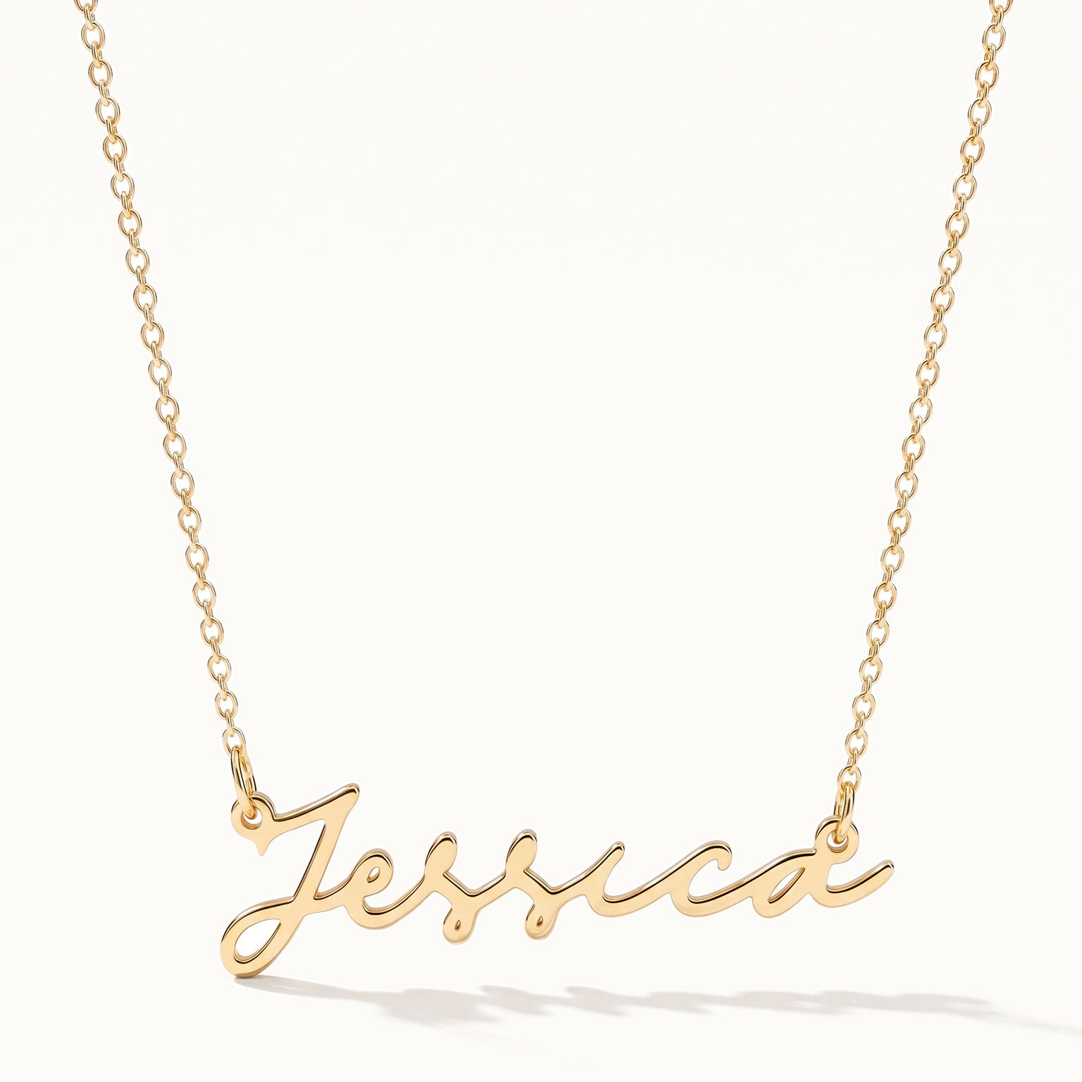Signature Name Necklace – name "Jessica" in script hanging on a fine chain, gold, on ivory background