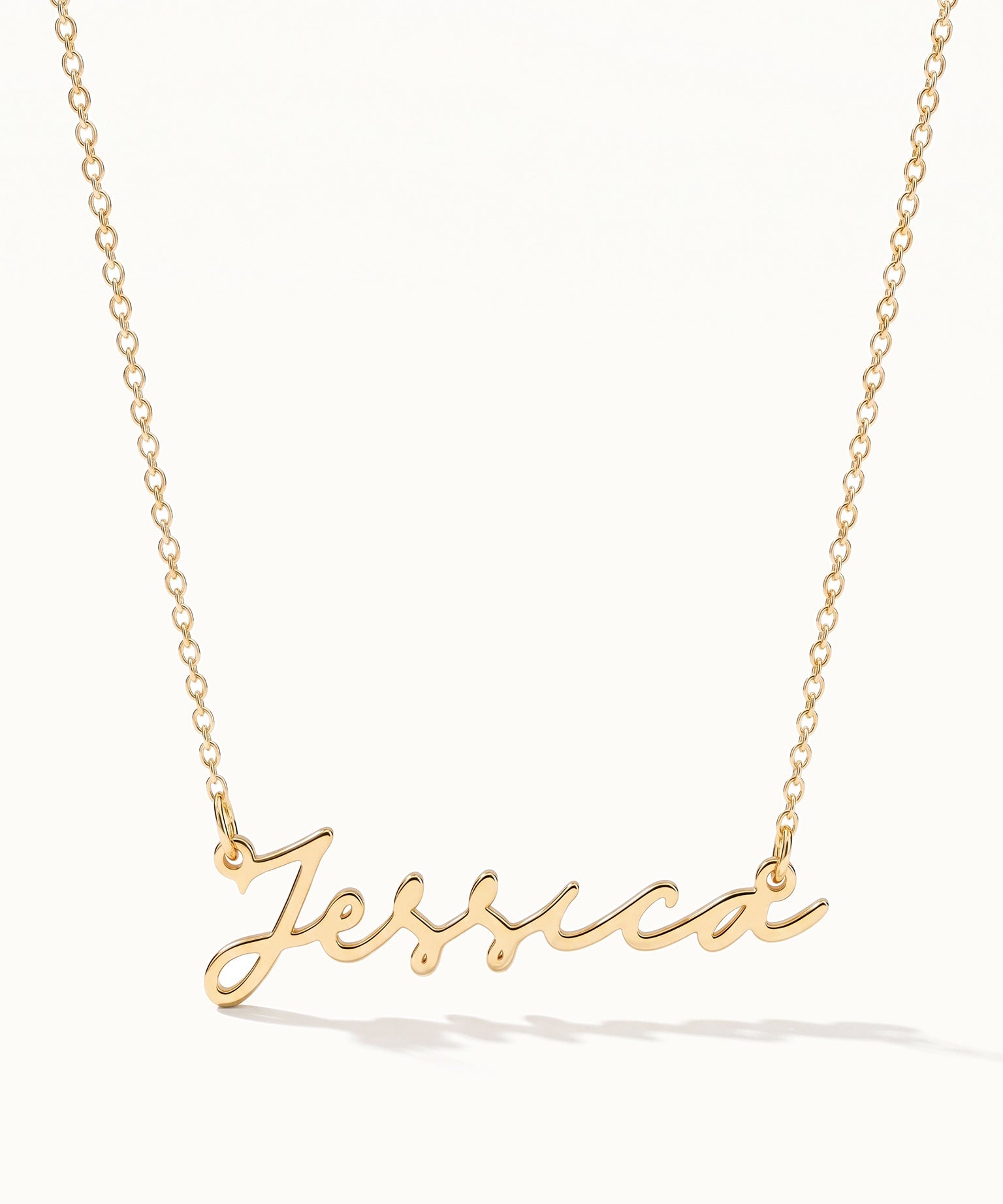 Signature Name Necklace – name "Jessica" in script hanging on a fine chain, gold, on ivory background