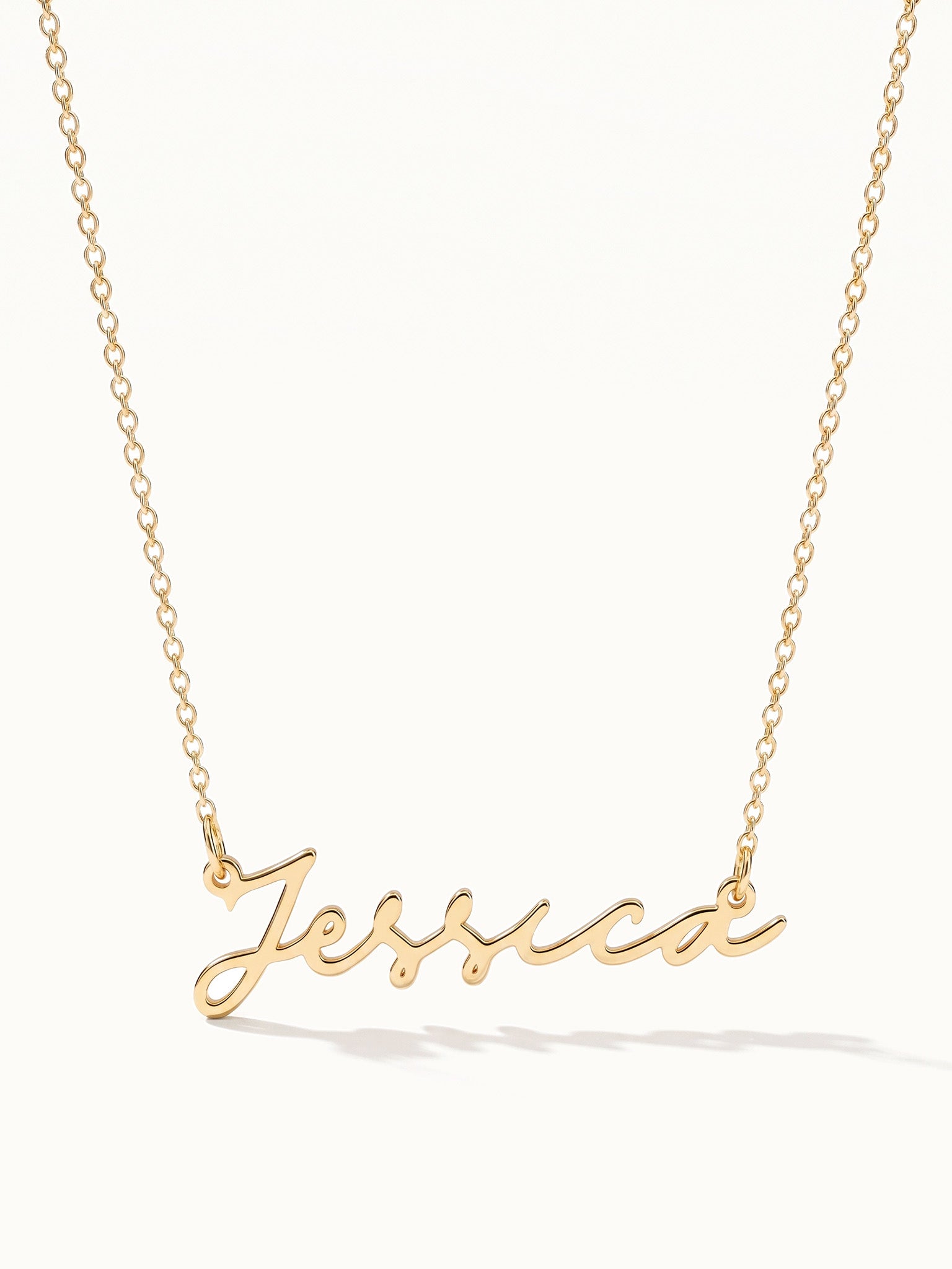 Signature Name Necklace – name "Jessica" in script hanging on a fine chain, gold, on ivory background