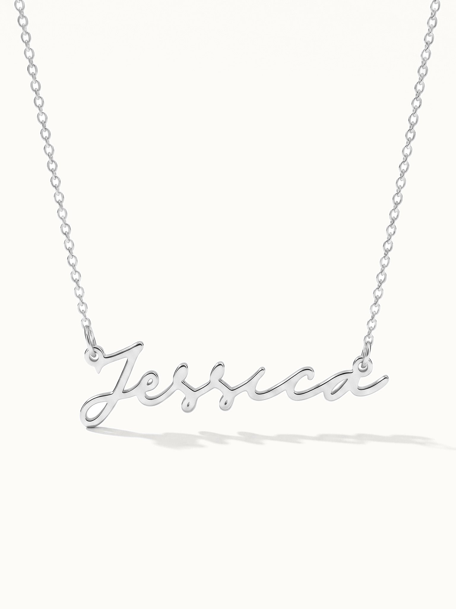 Signature Name Necklace – name "Jessica" in script hanging on a fine chain, closer view, silver, on ivory background