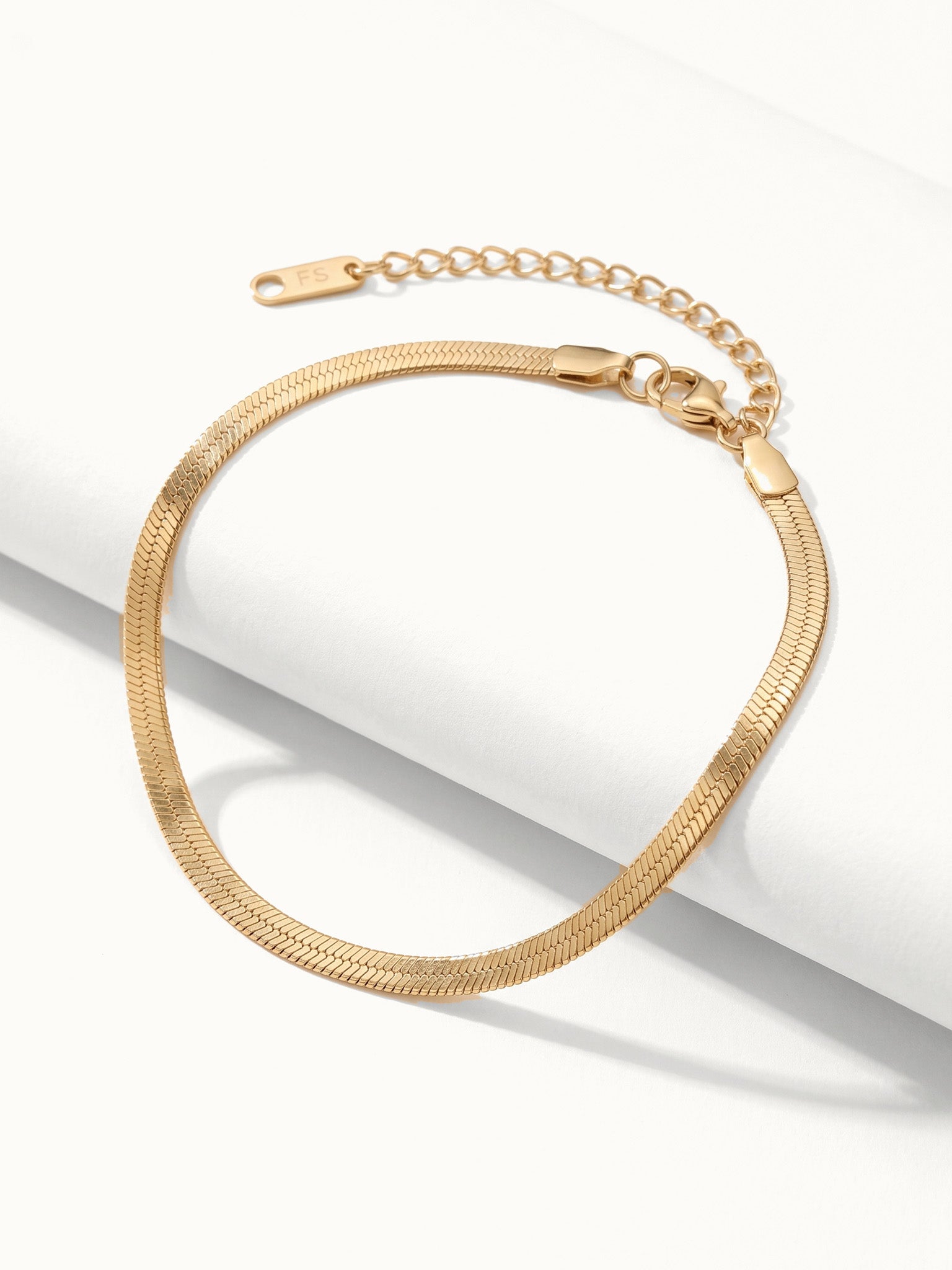 Still Waters Herringbone Bracelet – draped over a white step, gold, on ivory background