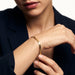 Still Waters Herringbone Bracelet – worn on the wrist, one hand adjusting the bracelet, gold, dark blazer, ivory studio background