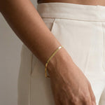 Still Waters Herringbone Bracelet – worn on the wrist, hand at the hip, gold, cream trousers