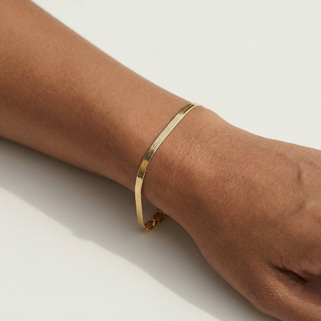 Still Waters Herringbone Bracelet – worn on the wrist, close-up, gold, on a light surface