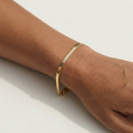 Still Waters Herringbone Bracelet – worn on the wrist, close-up, gold, on a light surface