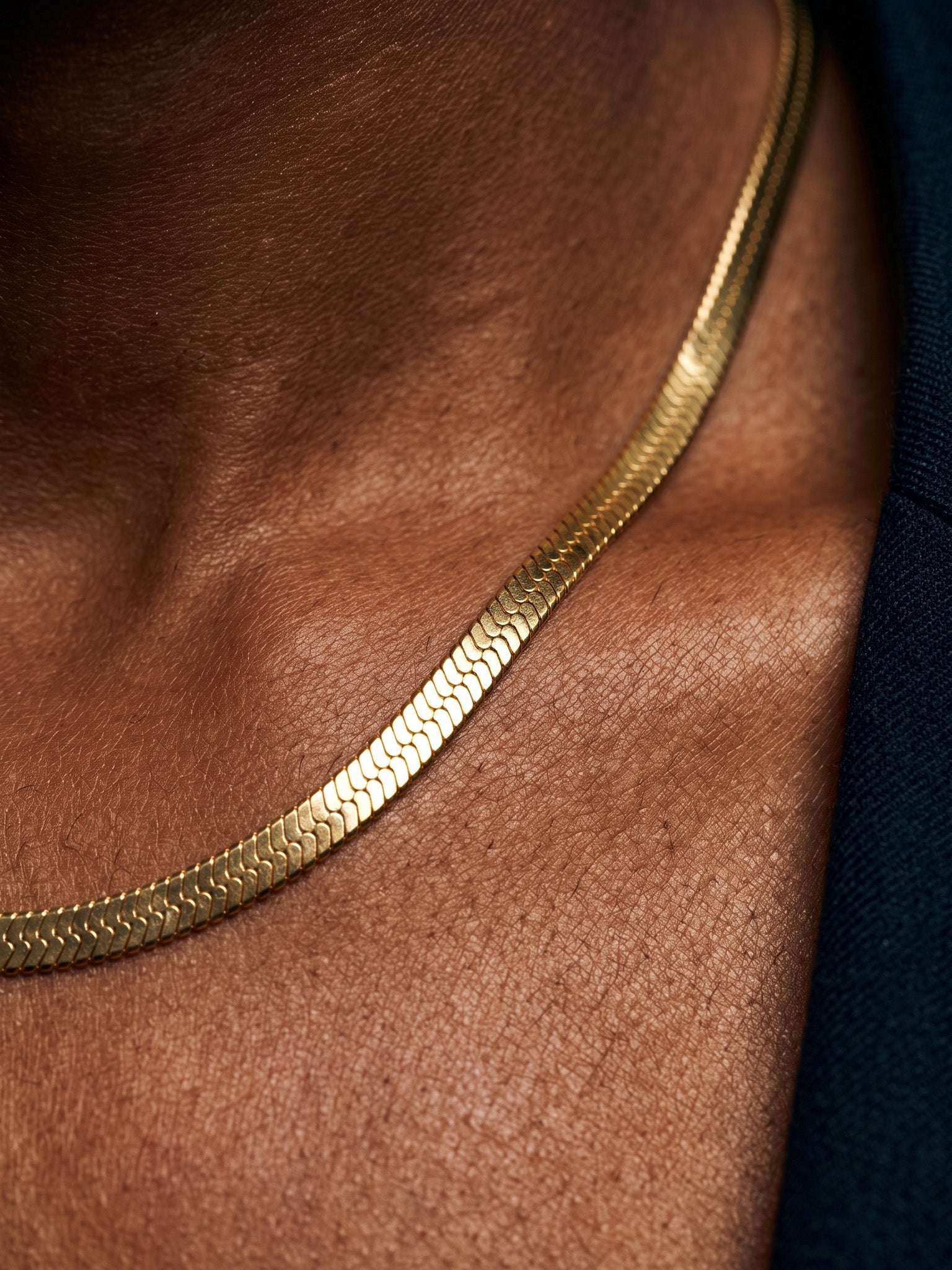 Fallen Herringbone Necklace – macro of the flat herringbone chain on the collarbone, gold