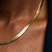 Fallen Herringbone Necklace – macro of the flat herringbone chain on the collarbone, gold