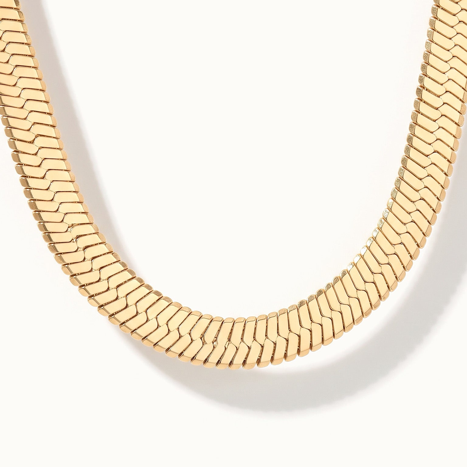 Sunday Best Herringbone Necklace – close-up of the wide herringbone chain at the bottom of the curve, gold, on ivory background