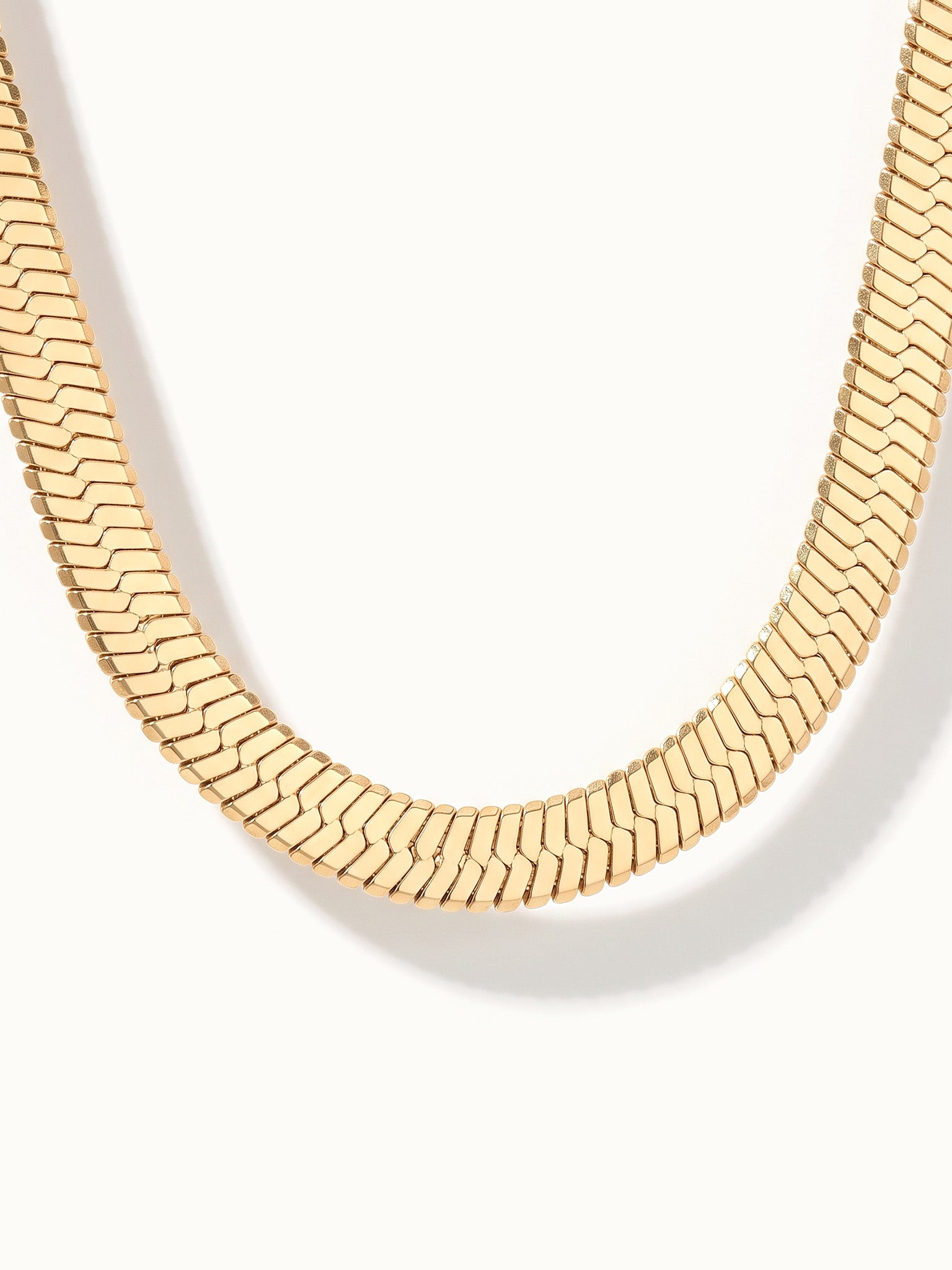 Fallen Herringbone Necklace – close-up of the wide herringbone chain at the bottom of the curve, gold, on ivory background