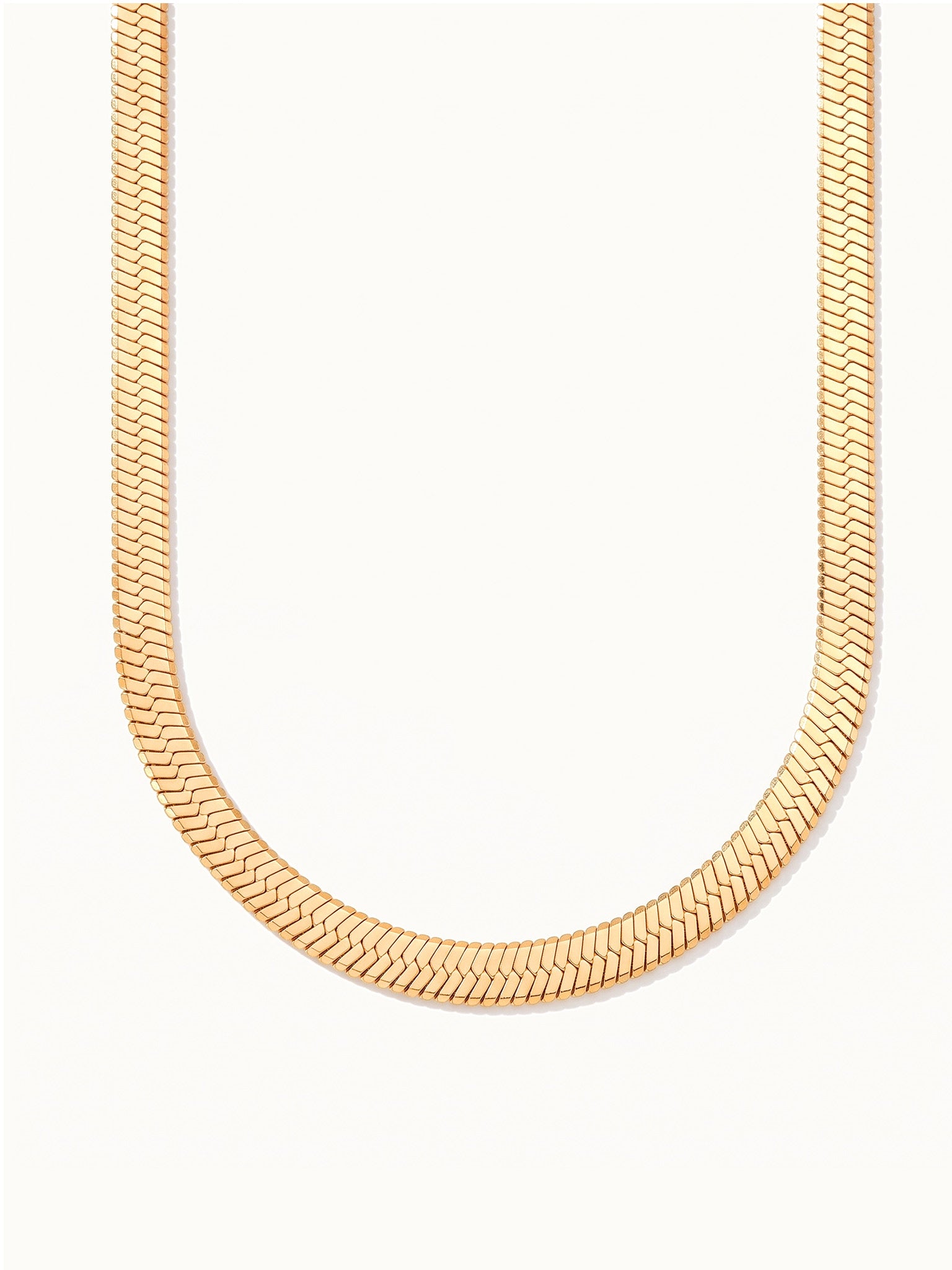 Fallen Herringbone Necklace – wide flat herringbone chain hanging in a drop, gold, on ivory background