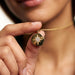 True North Necklace – star-compass medallion held between finger and thumb, close crop, gold, ivory studio background