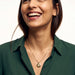 True North Necklace – worn at the chest, laughing, gold, deep green shirt, ivory studio background