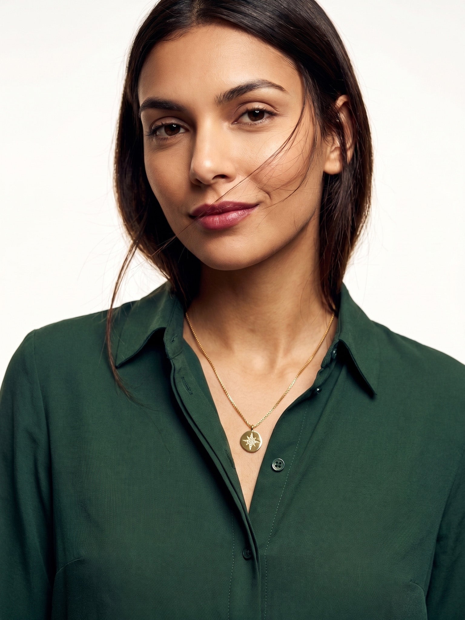True North Necklace – worn at the chest, calm look to camera, gold, deep green shirt, ivory studio background