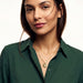 True North Necklace – worn at the chest, calm look to camera, gold, deep green shirt, ivory studio background