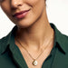 True North Necklace – worn at the chest, close crop of the star-compass medallion, gold, deep green shirt, ivory studio background