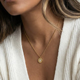 True North Necklace in gold held between two fingers, worn with a white cardigan