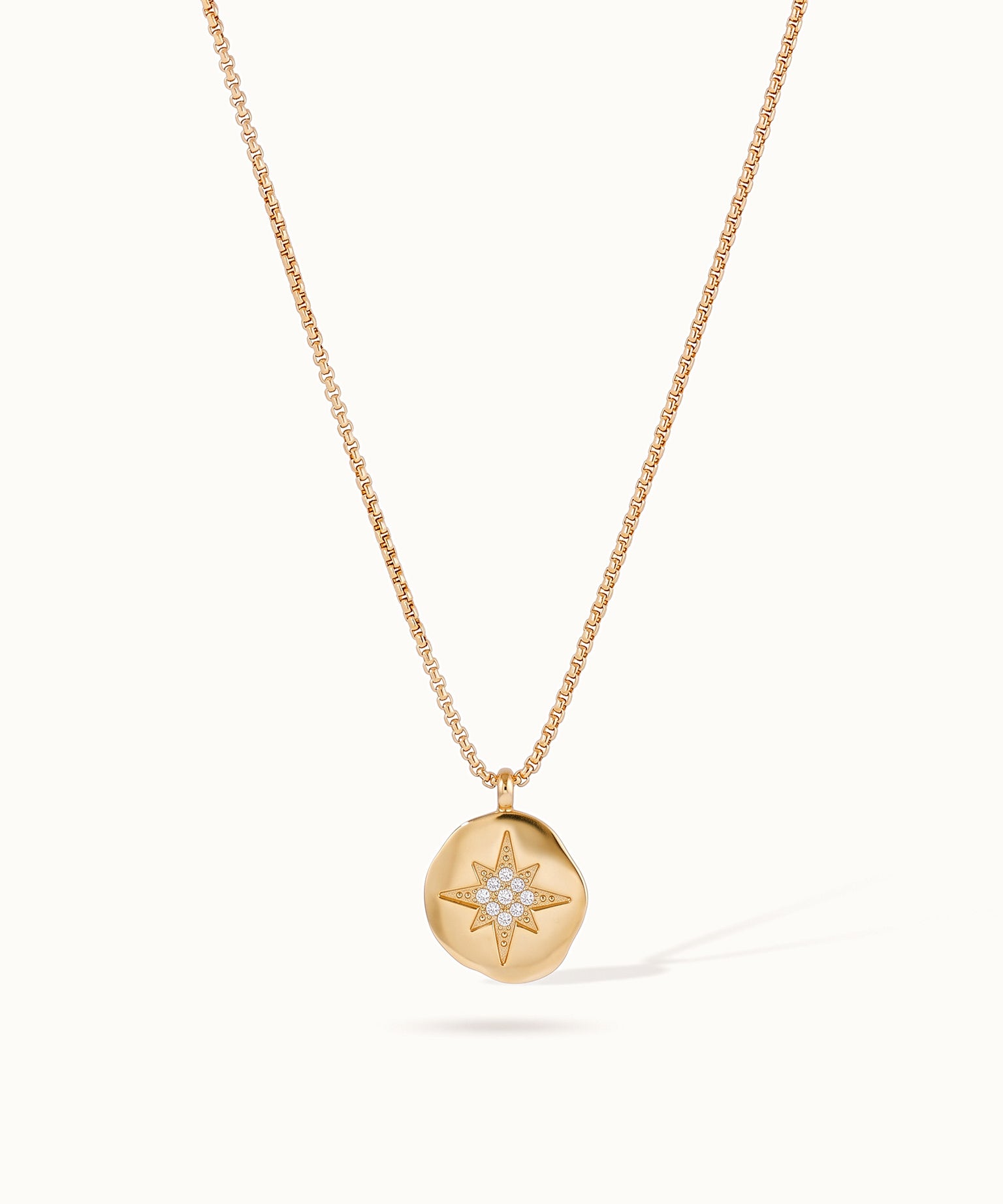 True North Necklace – star-compass medallion hanging on a box chain, gold, on ivory background