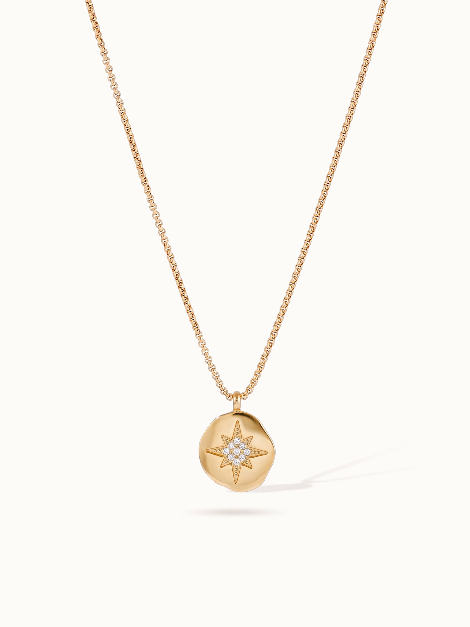 True North Necklace – star-compass medallion hanging on a box chain, gold, on ivory background