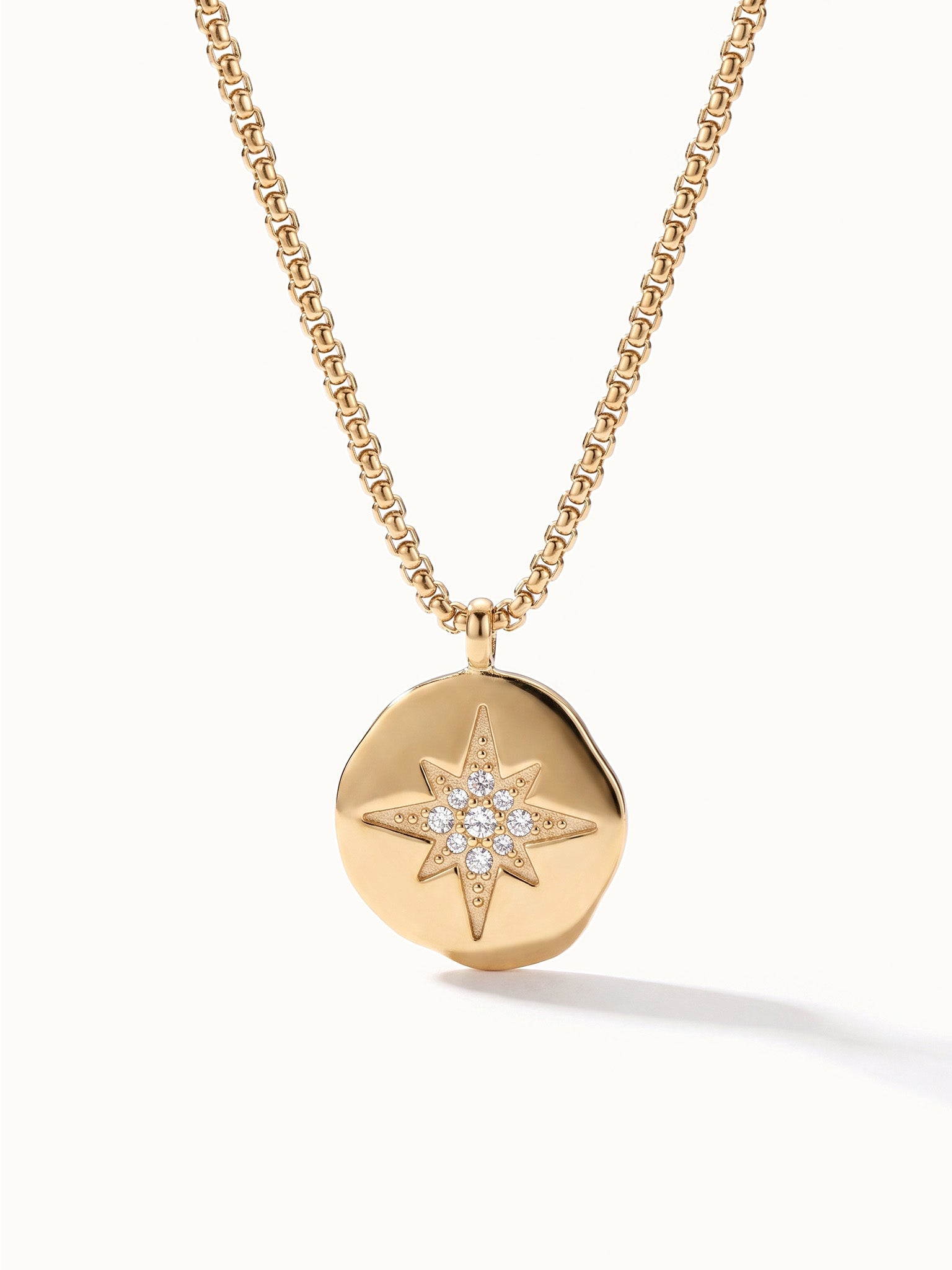 True North Necklace – close-up of the star-compass medallion with clear stones, gold, on ivory background